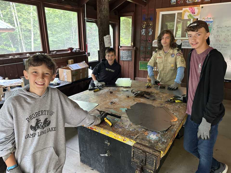 Some scouts surround a handicraft workbench with tools and materials atop it