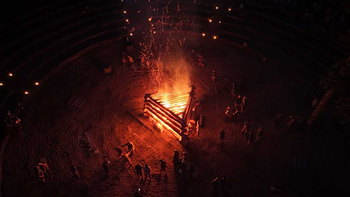 A triangular bonfire blazes in a central field with scouts moving around it