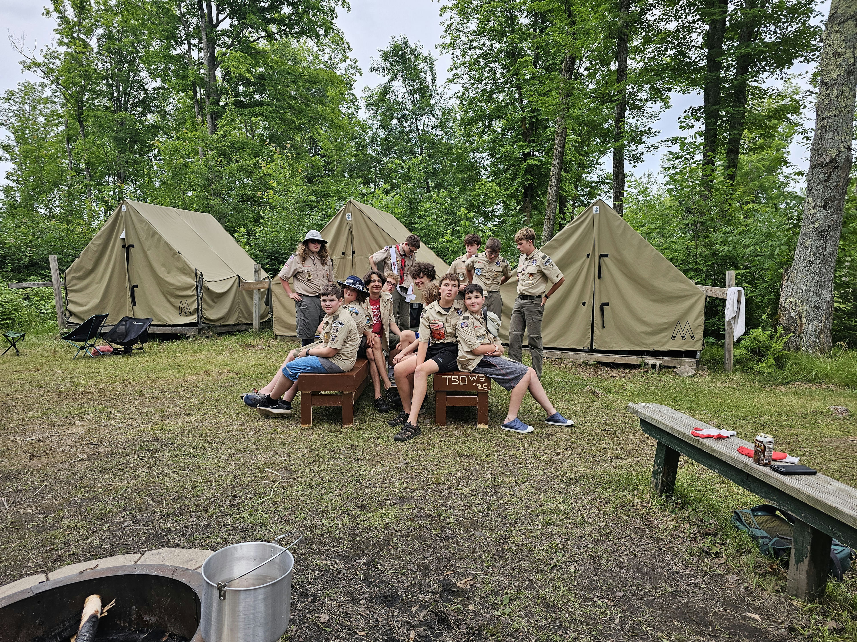 A group of scouts sits in front of tents at a campsite