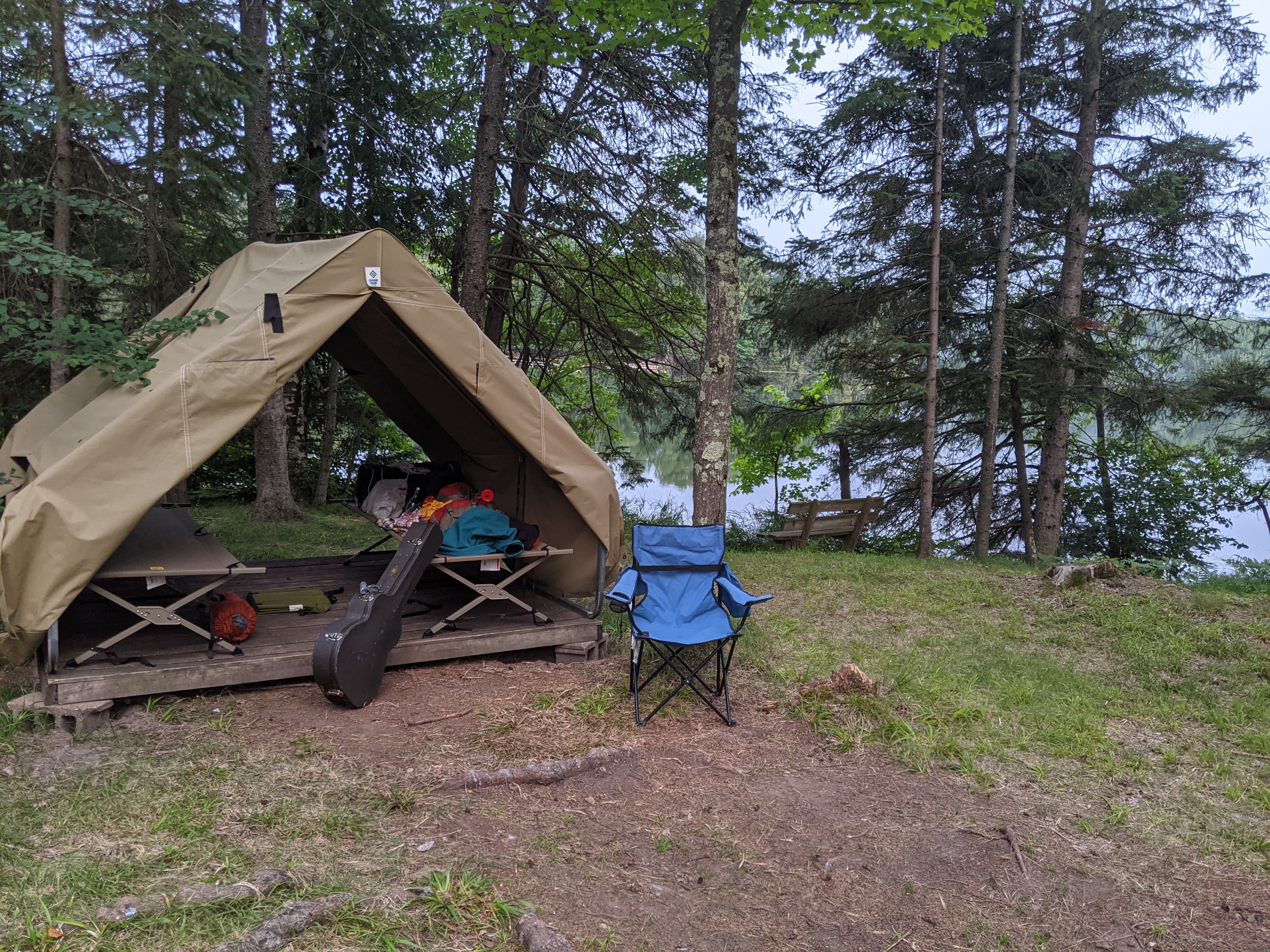 A tent with a chair in front of it, a guitar case and a number of other tools and packs are displayed.