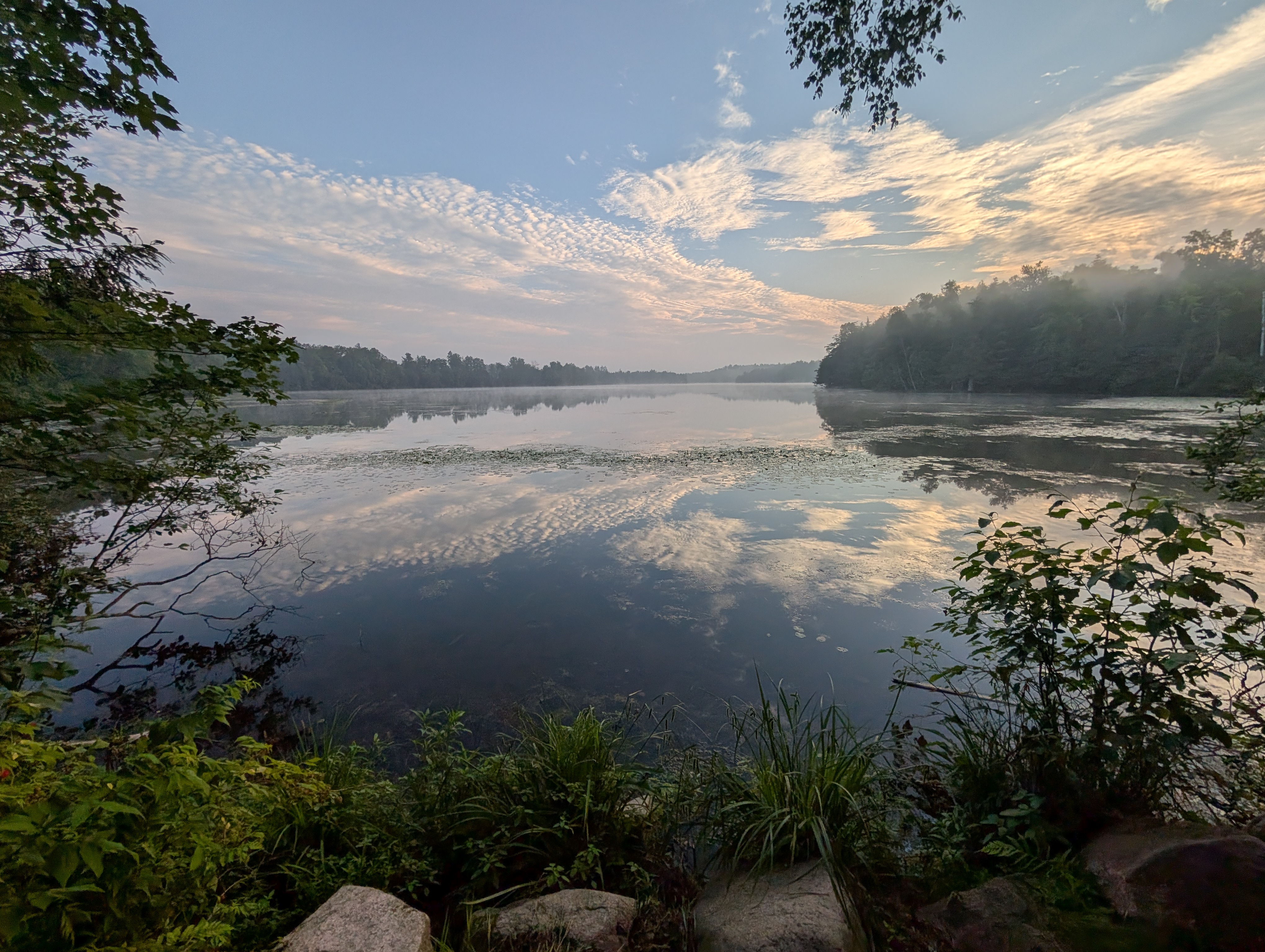 The lake is seen from the shore, with the bright blue sky reflecting off the clear waters