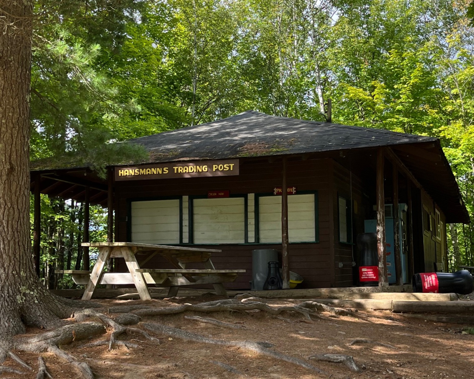 The East Trading post is a small log cabin with a roofed over porch area and a park bench in front of it.