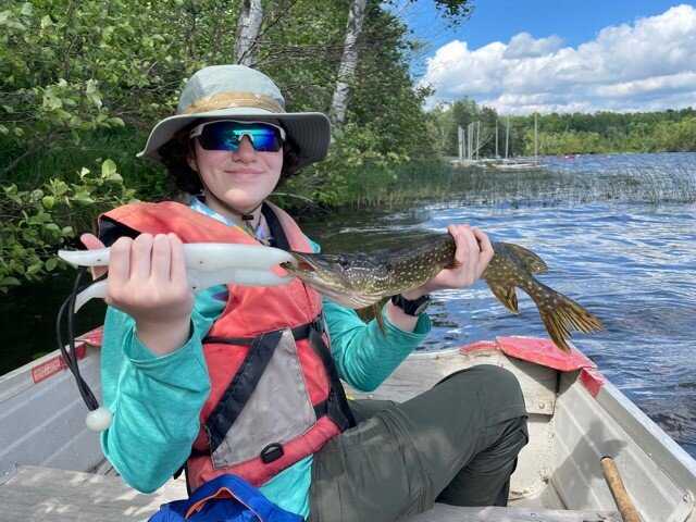 A woman sits on a boat and holds up her catch - a large fish!