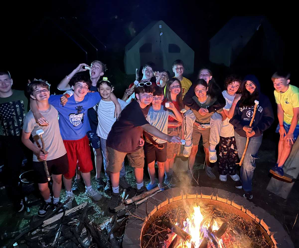 A bunch of smiling scouts cook marsh mellows over a fire pit