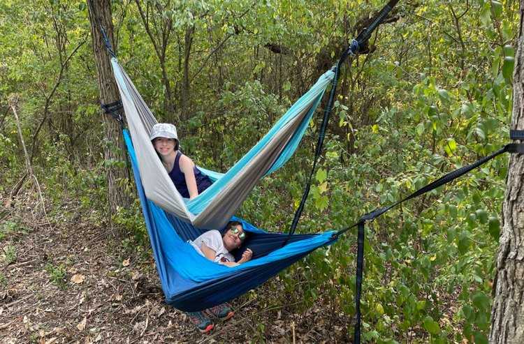 Two girls hanging out in hammocks, with beautiful lush green forest behind them