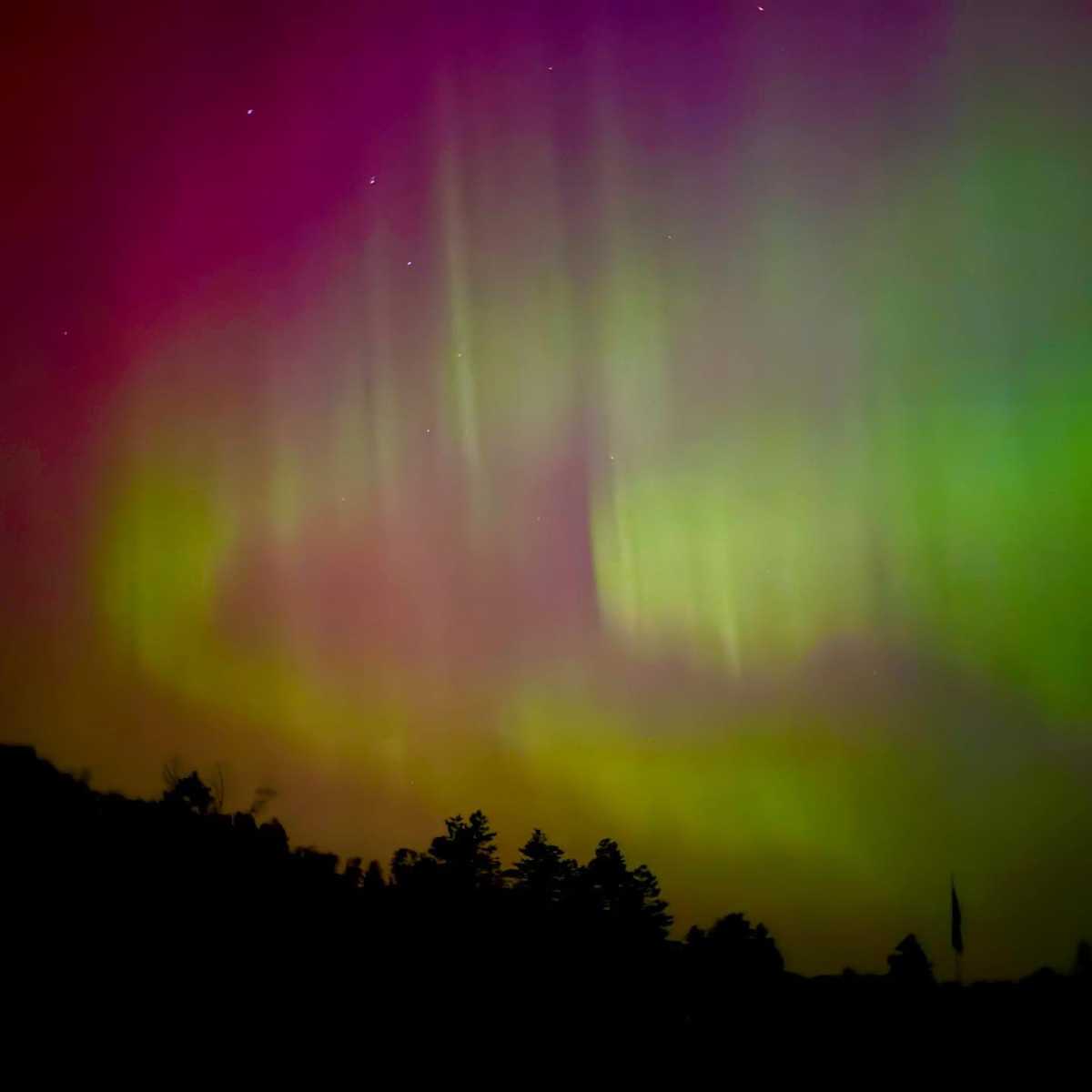 The northern lights glow pink and green against the dark night sky above Camp MaKaJaWan