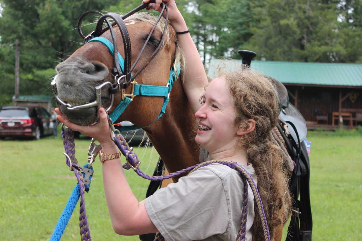 A girl smiles brightly while putting the reins on a horse